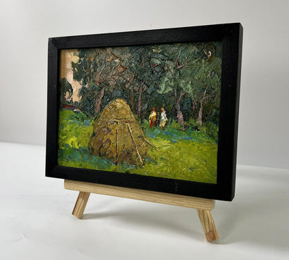 Oil painting of haystack near forest by Oksana Ivanyuk in black frame on easel