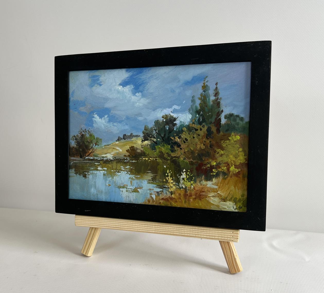 Black-framed oil painting by Yuriy Suprunchuk of serene lakeside on wooden easel