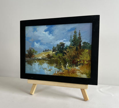 Black-framed oil painting by Yuriy Suprunchuk of serene lakeside on wooden easel