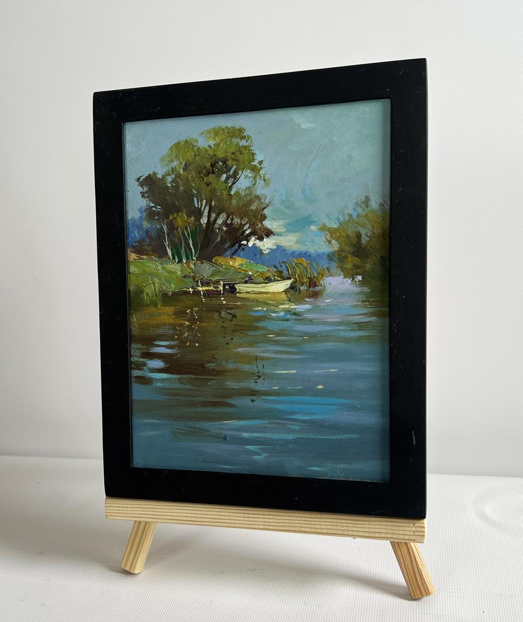 Black-framed oil painting of serene river with boat by Yuriy Suprunchuk on easel