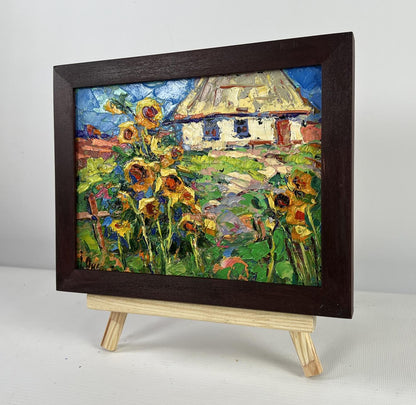 Vibrant impressionist oil painting of sunflowers and cottage by Oksana Ivanyuk in wooden frame