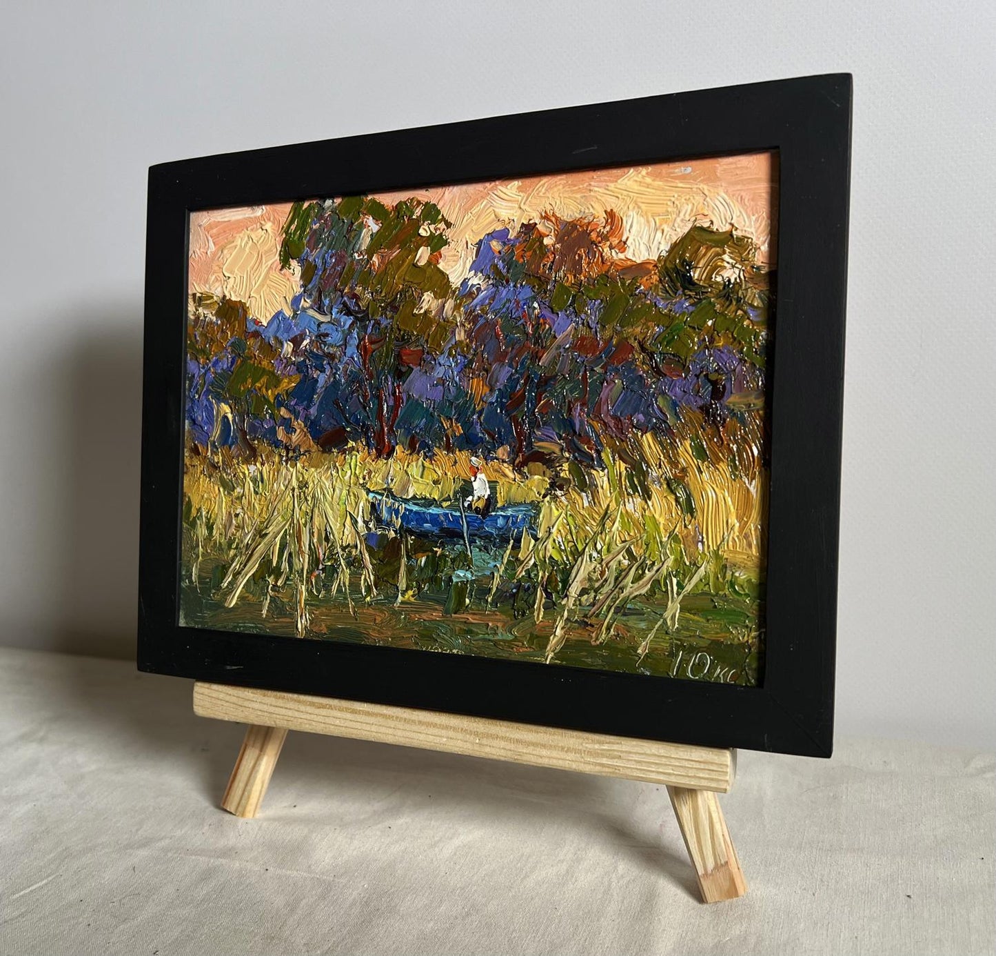 Oil painting of blue boat among golden reeds by Oksana Ivanyuk in black frame