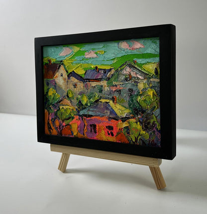 Oil painting of village houses by Oleksiy Ivanyuk in black frame on easel