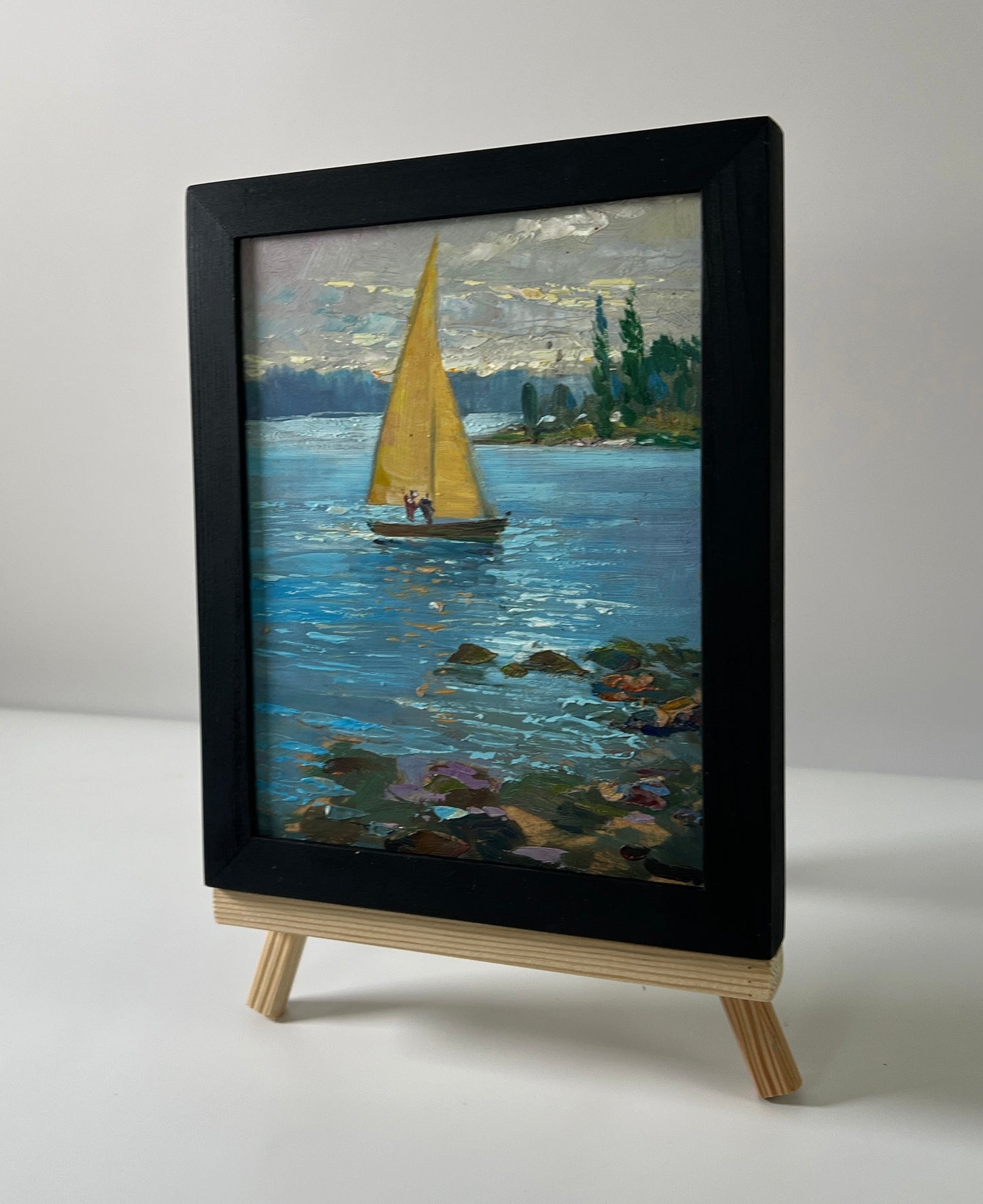 Oil painting of yellow-sailed boat on river by Yuriy Suprunchuk in black frame