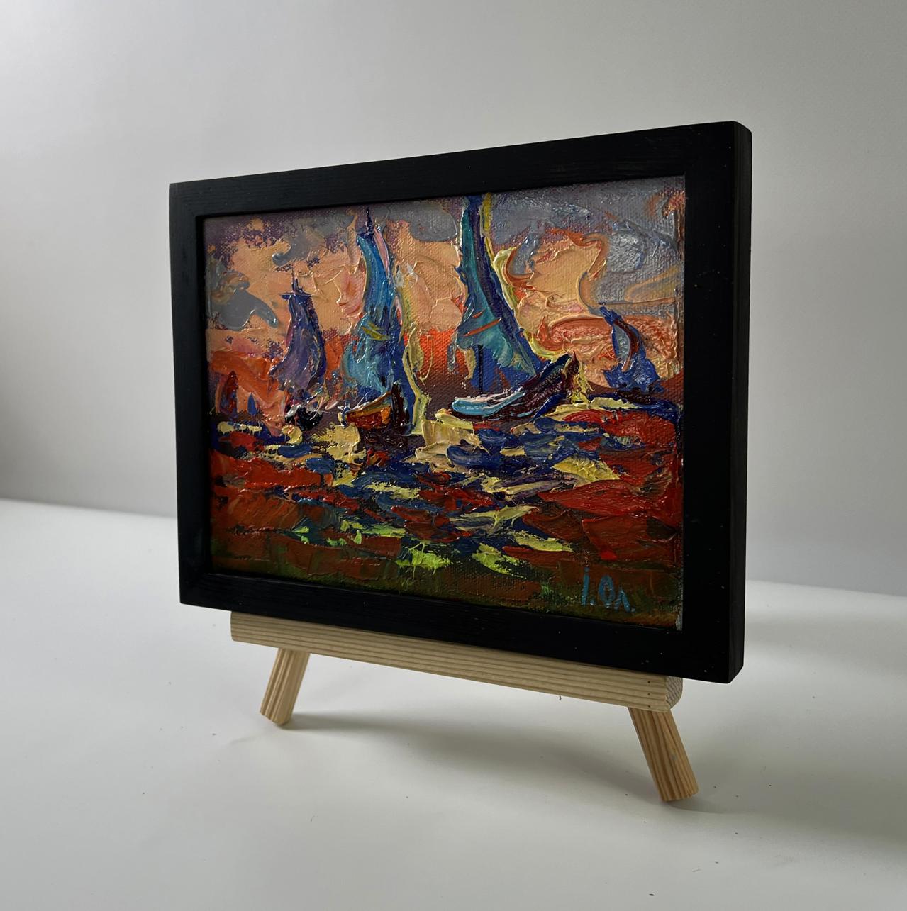 Oil painting of sailboats and orange sunset by Oleksiy Ivanyuk in black frame on easel