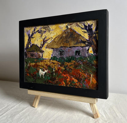 Black-framed oil painting by Oleksiy Ivanyuk: yellow sunset behind rustic village houses