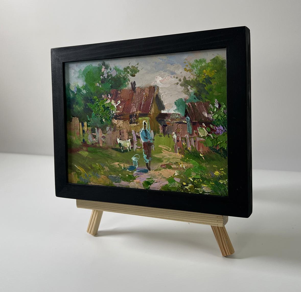 Black-framed oil painting of rustic village yard by Yuriy Suprunchuk on wooden easel