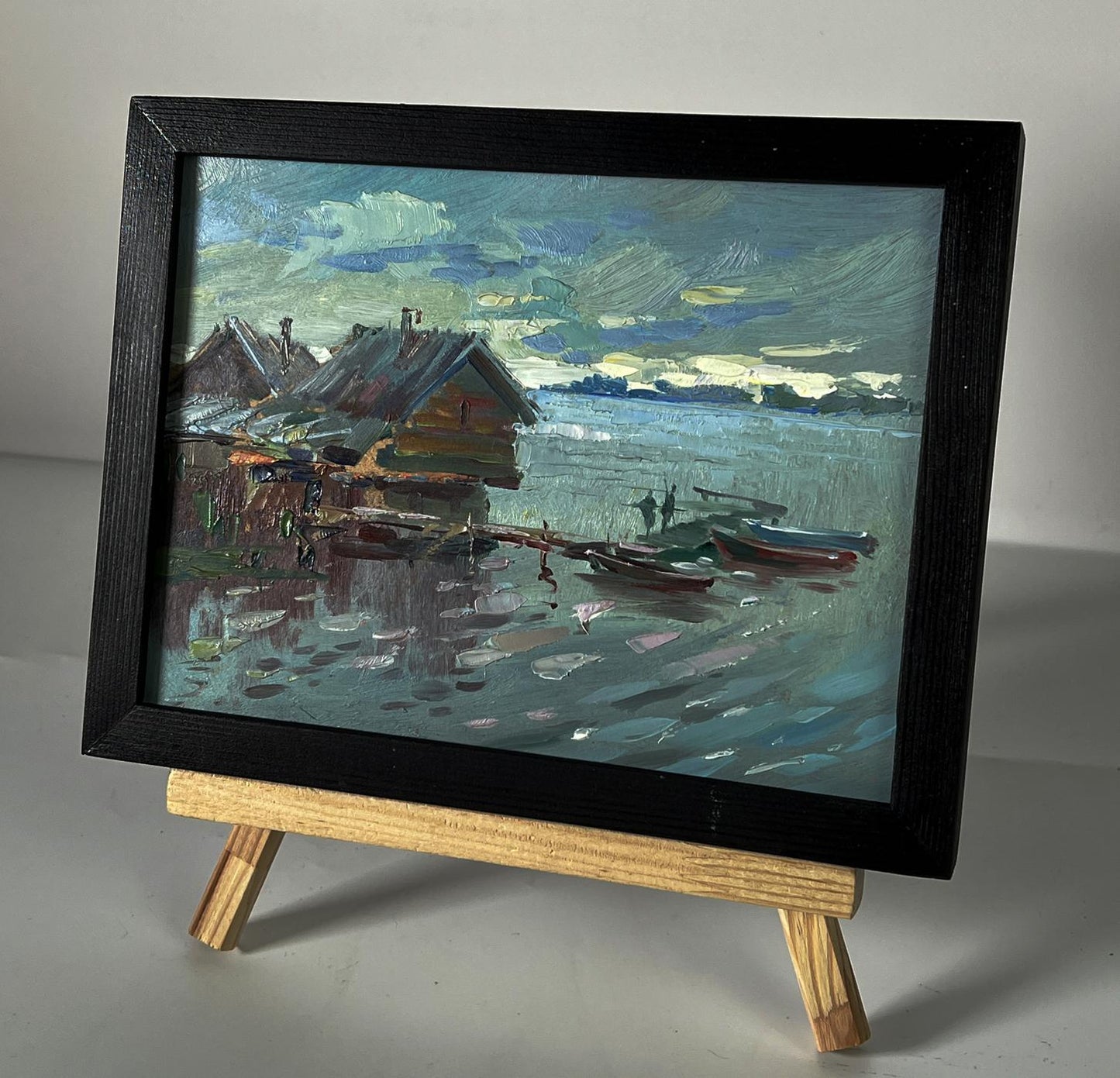 Framed oil painting of serene lakeside houses on water by Yuriy Suprunchuk