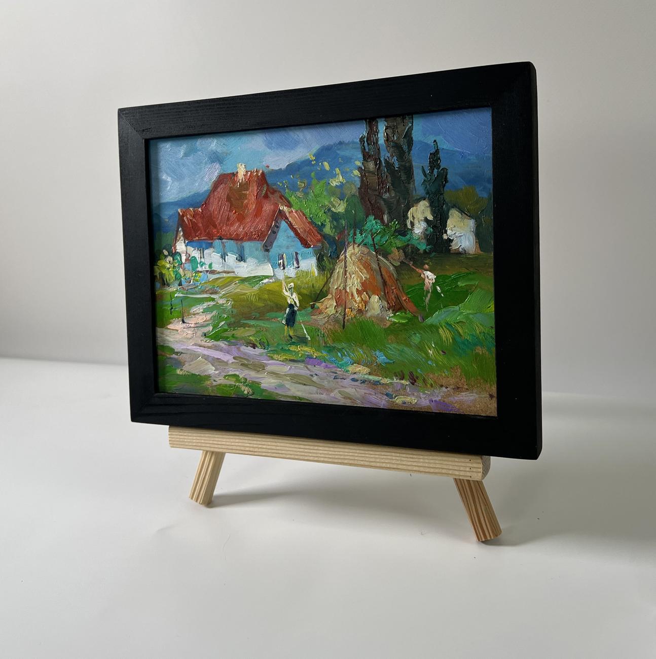 Black-framed miniature oil painting of village near mountains by Yuriy Suprunchuk on wooden easel
