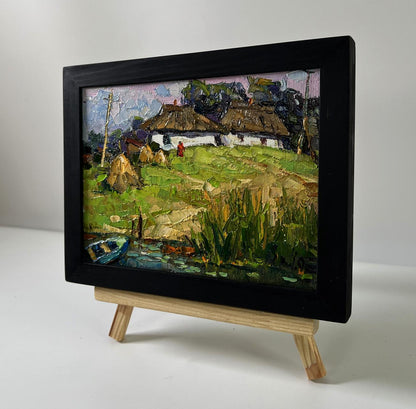 Black-framed oil painting Village near the swamps by Oksana Ivanyuk on easel