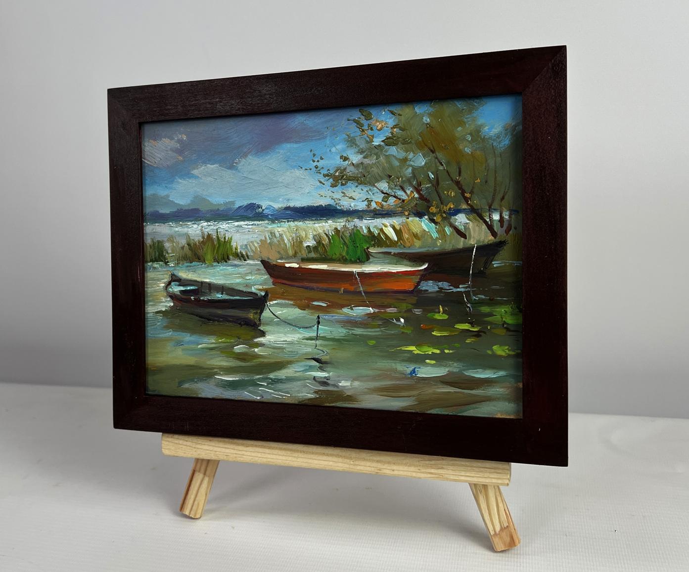Dark wooden-framed oil painting of boats moored on shore by Yuriy Suprunchuk