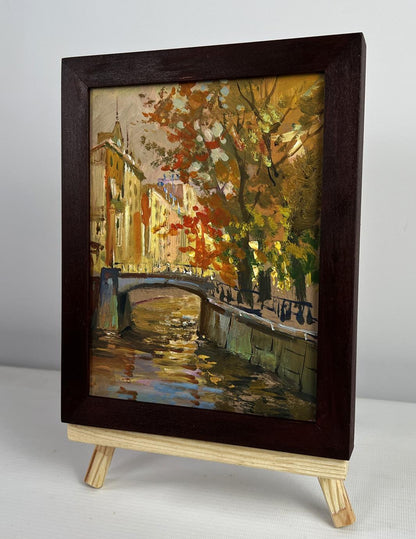 Dark wood-framed oil painting of autumn canal park by Yuriy Suprunchuk on easel
