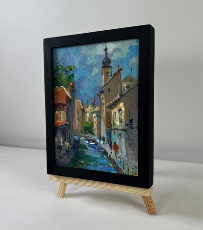 Black-framed miniature oil painting of Yuriy Suprunchuk city street on easel