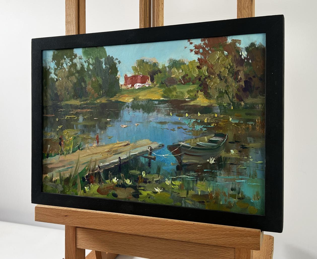 Black-framed oil painting of serene lakeside boat in lumber mill by Yuriy Suprunchuk