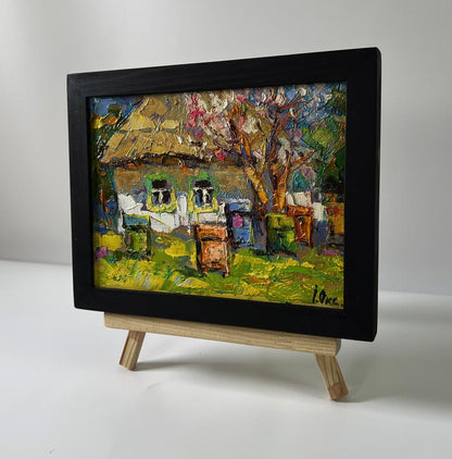Oil painting House in the village by Oksana Ivanyuk in black frame on easel