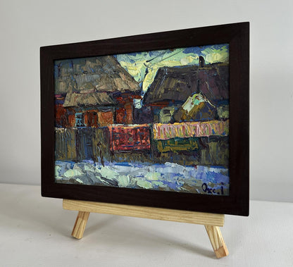 Oil painting by Oksana Ivanyuk: sunset behind village rooftops on easel