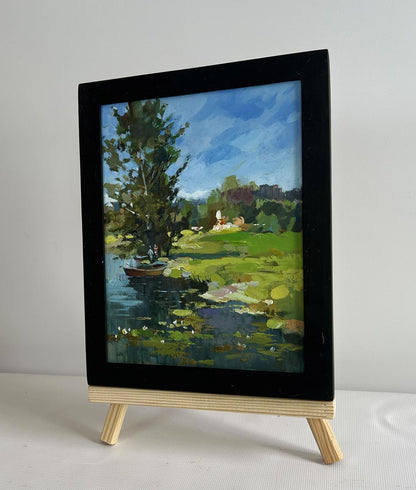 Black-framed oil painting of serene pond with lily pads, boat by lonely tree by Yuriy Suprunchuk