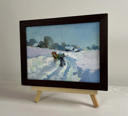 Dark wooden-framed miniature oil painting of snowy landscape with horse-drawn sled by Yuriy Suprunchuk on light wood easel