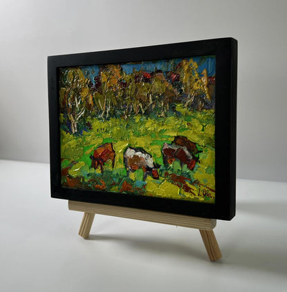Oil painting of cows grazing in meadow by Oksana Ivanyuk in black frame