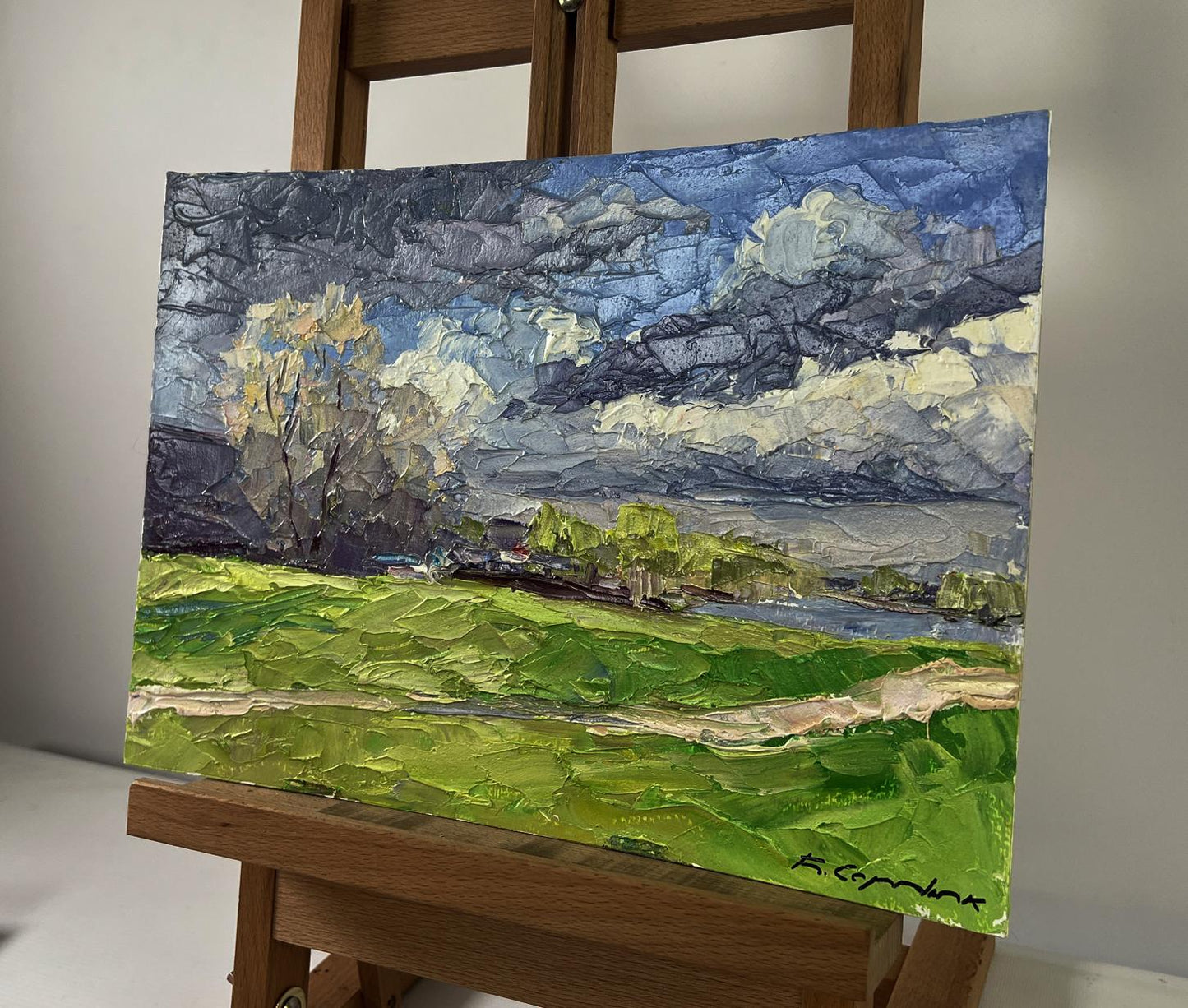 Oil painting The first rays of warm by Boris Serdyuk: vibrant green fields, river, dramatic clouds