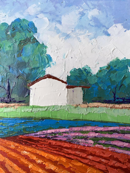 A white painted barn with a reddish-brown roof nestled among lush green trees under a textured blue and white sky.