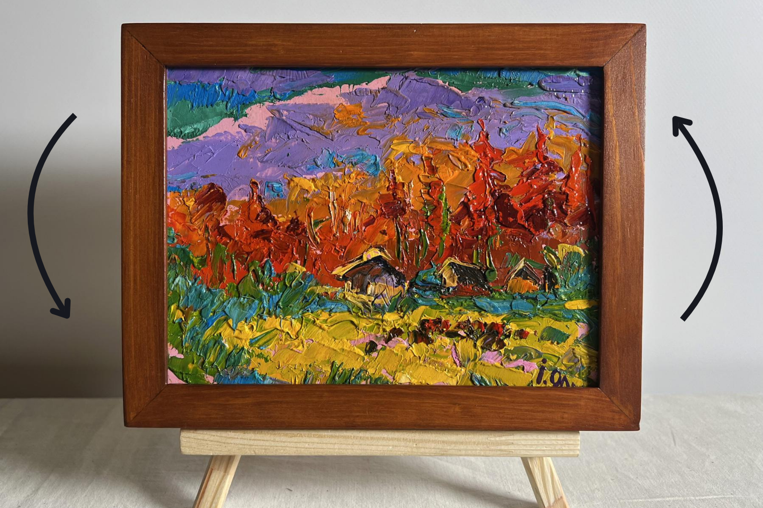 A vibrant, textured oil painting in a rustic wooden frame depicts autumnal hills and cabins with bold strokes of orange, purple, red, green, and yellow.