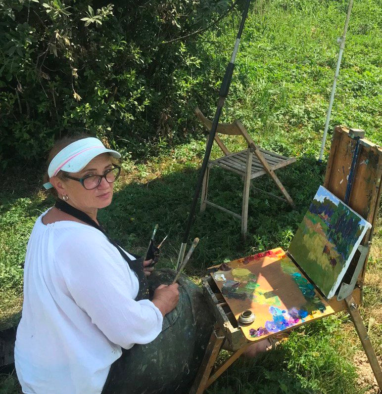A wooden easel holding a partially completed landscape painting with vibrant greens, blues, and earth tones.