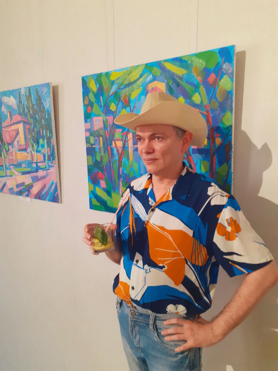 Man wearing a beige cowboy hat and a blue, white, and orange floral-patterned short-sleeve shirt