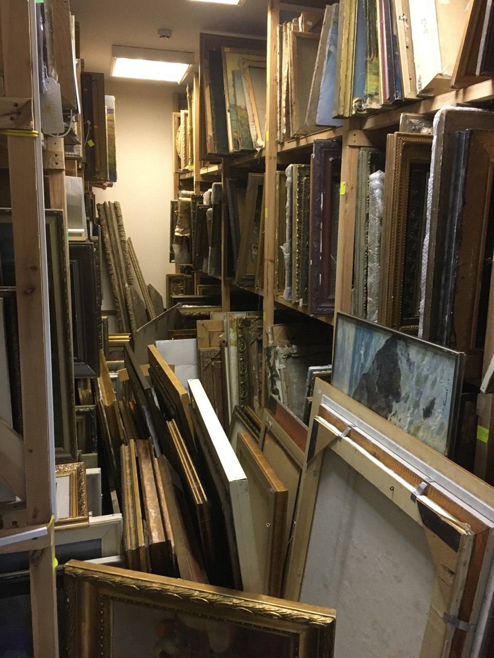 Ornate gold-framed paintings stacked in cluttered storage for wholesale