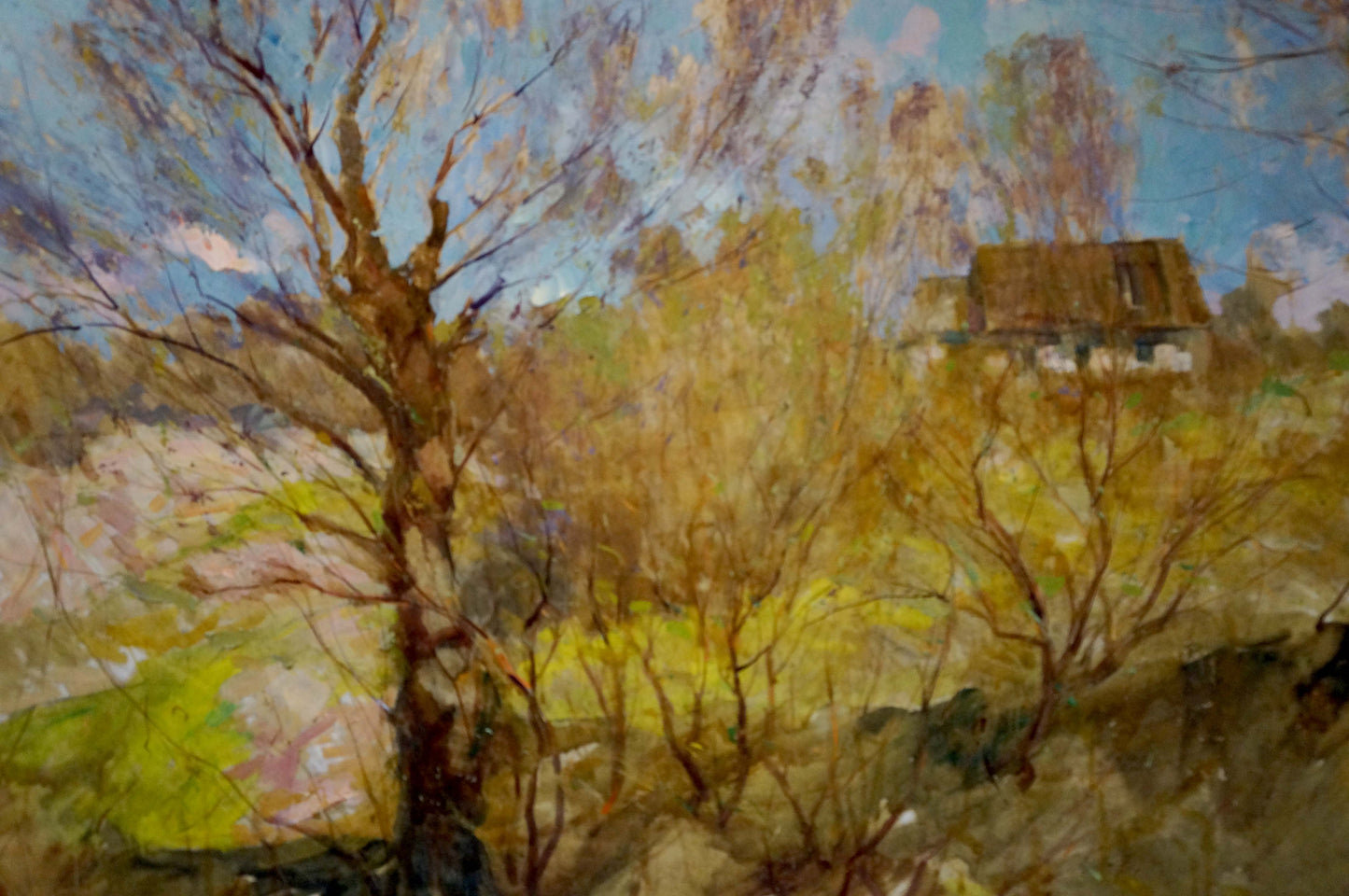 A rustic wooden house with a thatched roof nestled among bare, autumnal trees under a soft blue sky.