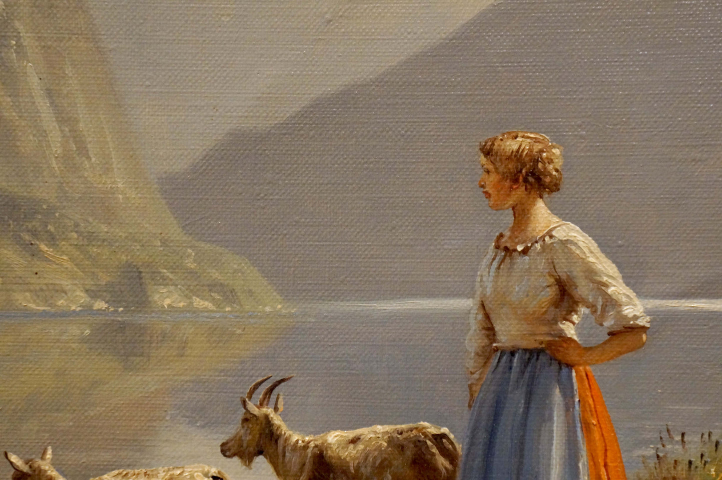 Oil painting by Louis Böhm: woman in white blouse, blue skirt, orange sash with goats by water