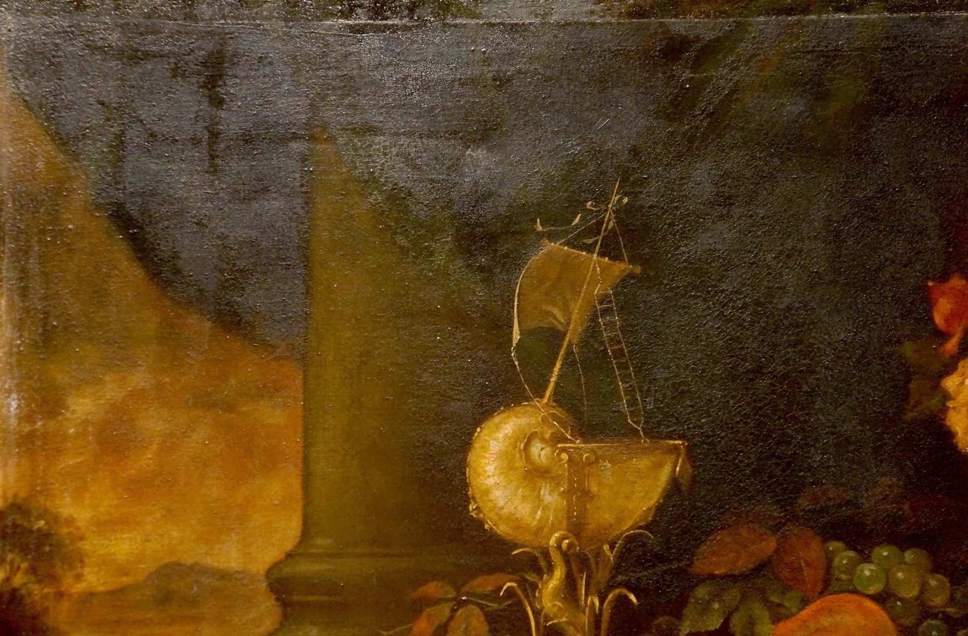 Golden nautilus shell with miniature sailboat atop oil painting