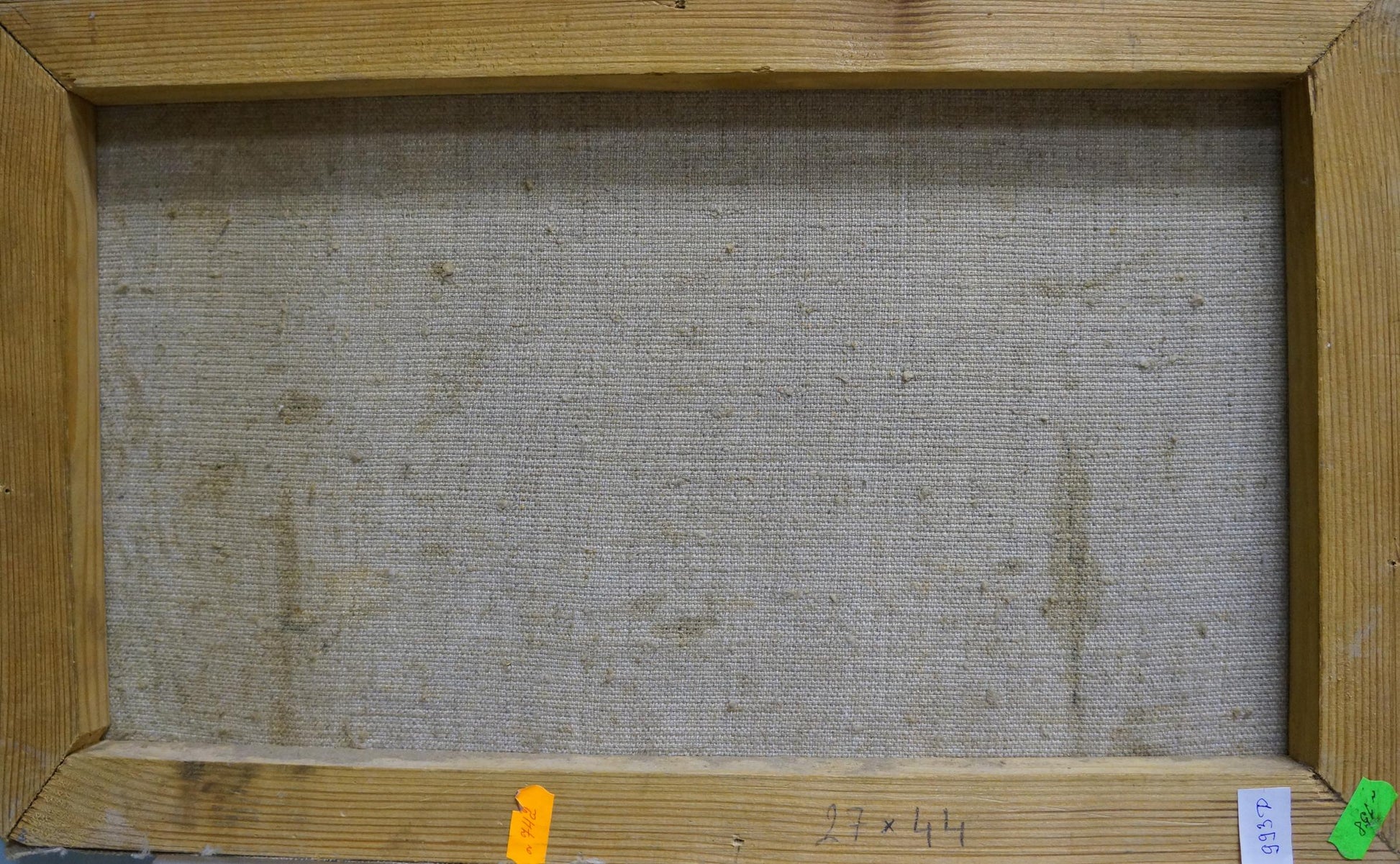 The back of a rectangular canvas painting with a light brown wooden frame and a textured, off-white fabric backing.