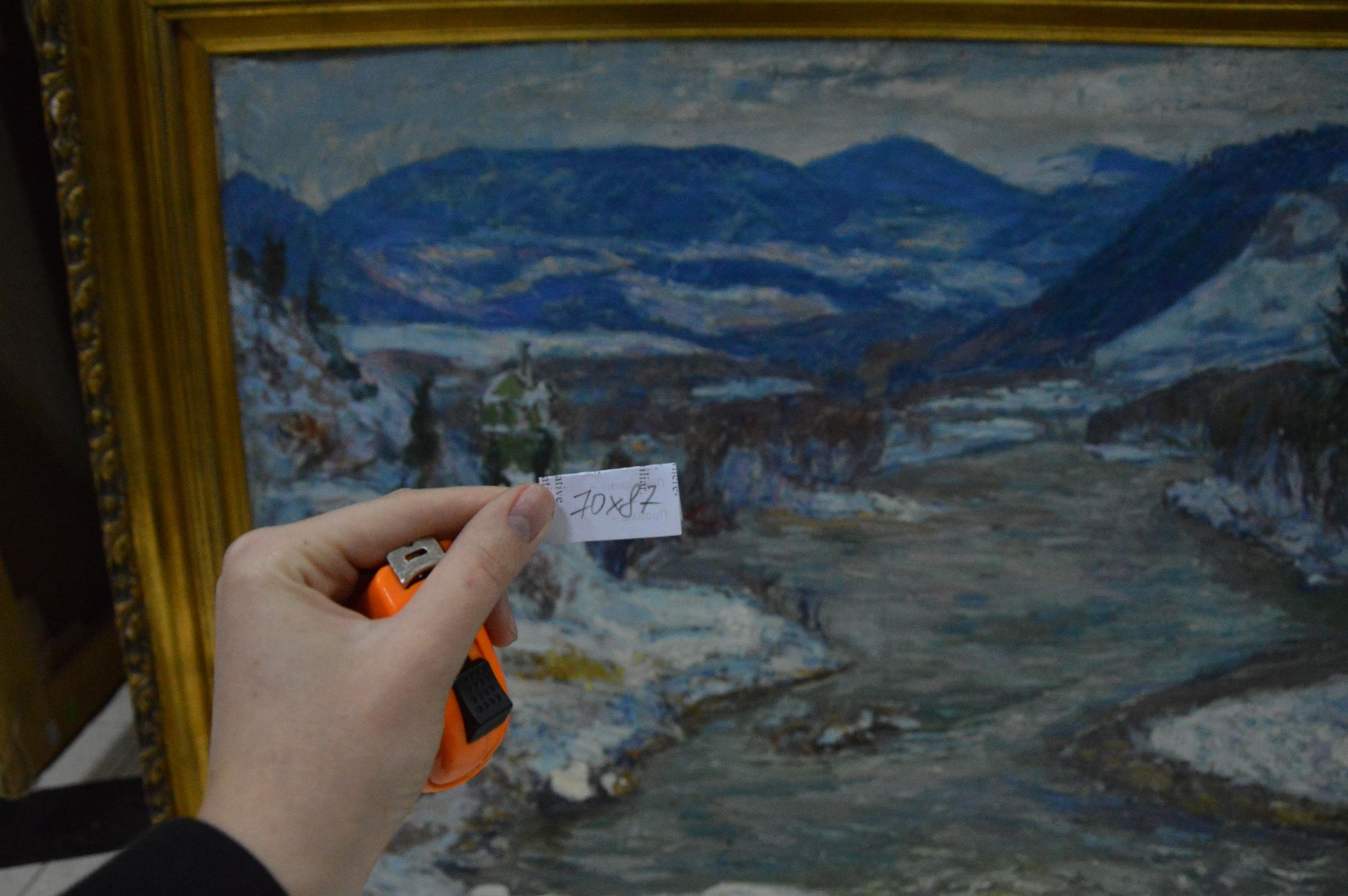 Hand holding tape measure labeled 70x82 in front of Kontratovich Winter landscape oil painting