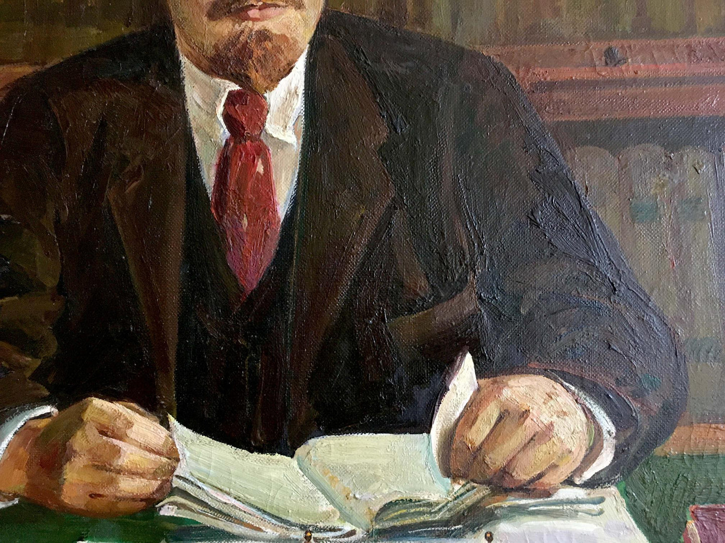 Oil painting of Lenin at table in dark suit and red tie holding book