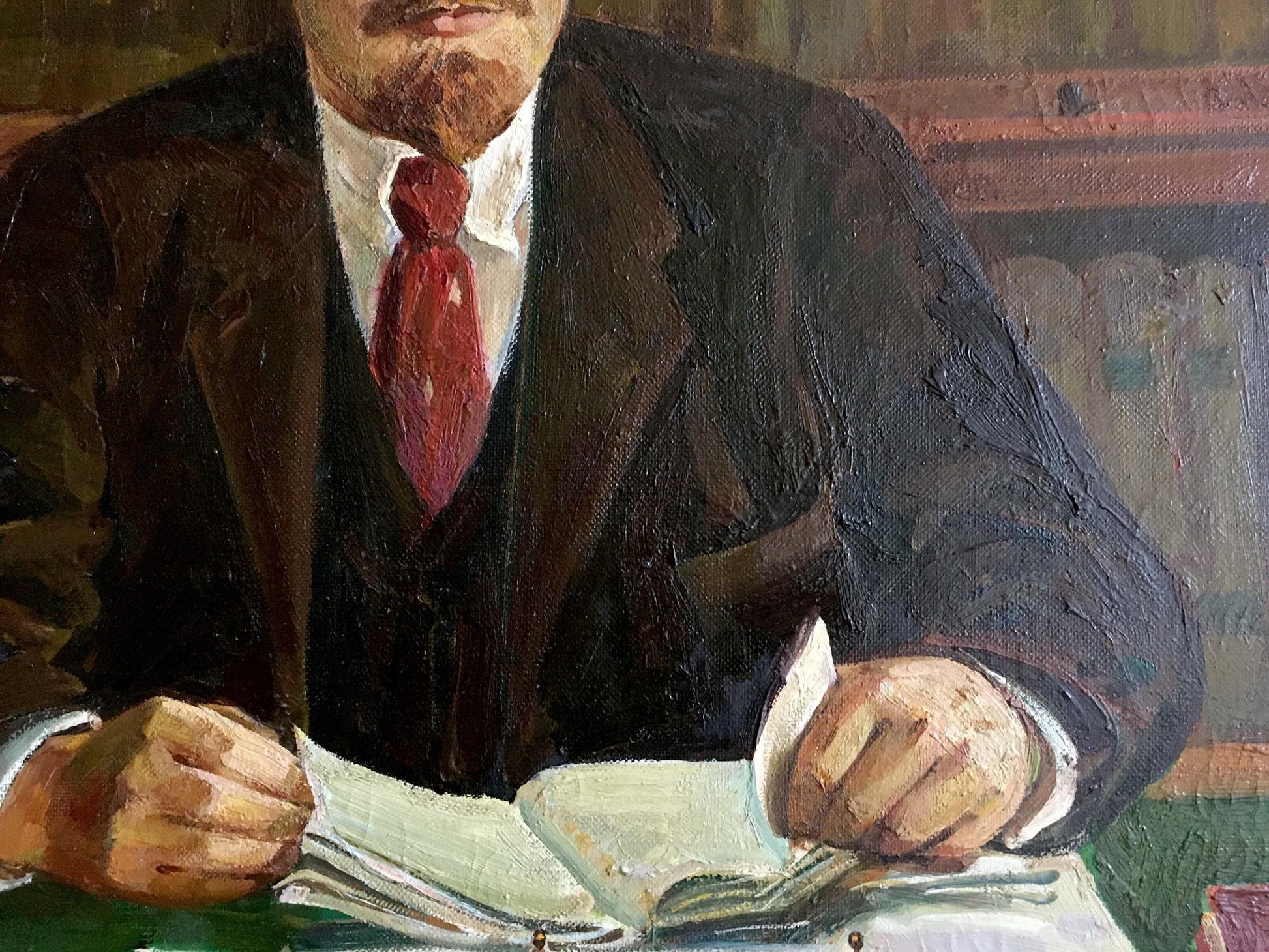 Oil painting of Lenin at table in dark suit and red tie holding book